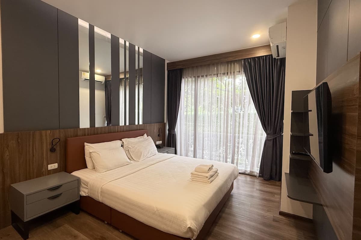 A modern hotel room with a large bed, a bedside table, a TV, and a window with curtains.