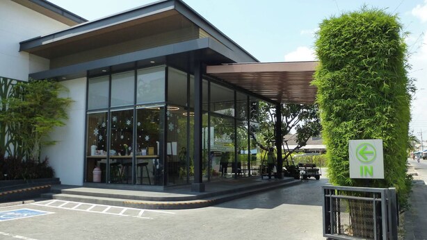 A modern building with large glass windows, a covered entrance, and a green sign indicating an indoor area. - The River Kwai Bridge Resort 2 (Kanchanaburi)