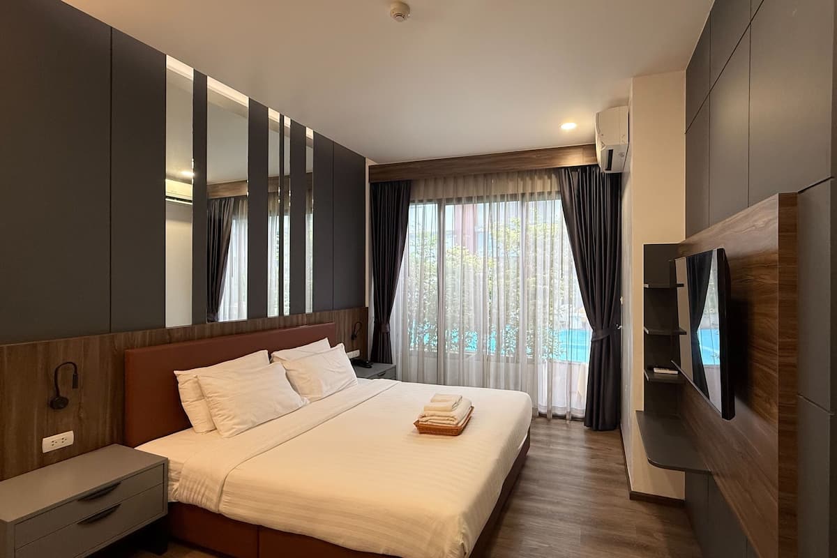 A modern hotel room with a large bed, a TV mounted on the wall, and a window with curtains.