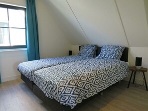 Ein Schlafzimmer mit Bett, einem Fenster mit Vorhängen, einem Nachttisch und einem Lautsprecher.