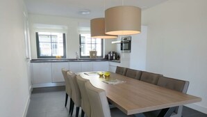A modern kitchen with white cabinets, a wooden dining table, and two pendant lights. - Holiday Home in Uitdam With Wi-fi (Uitdam)