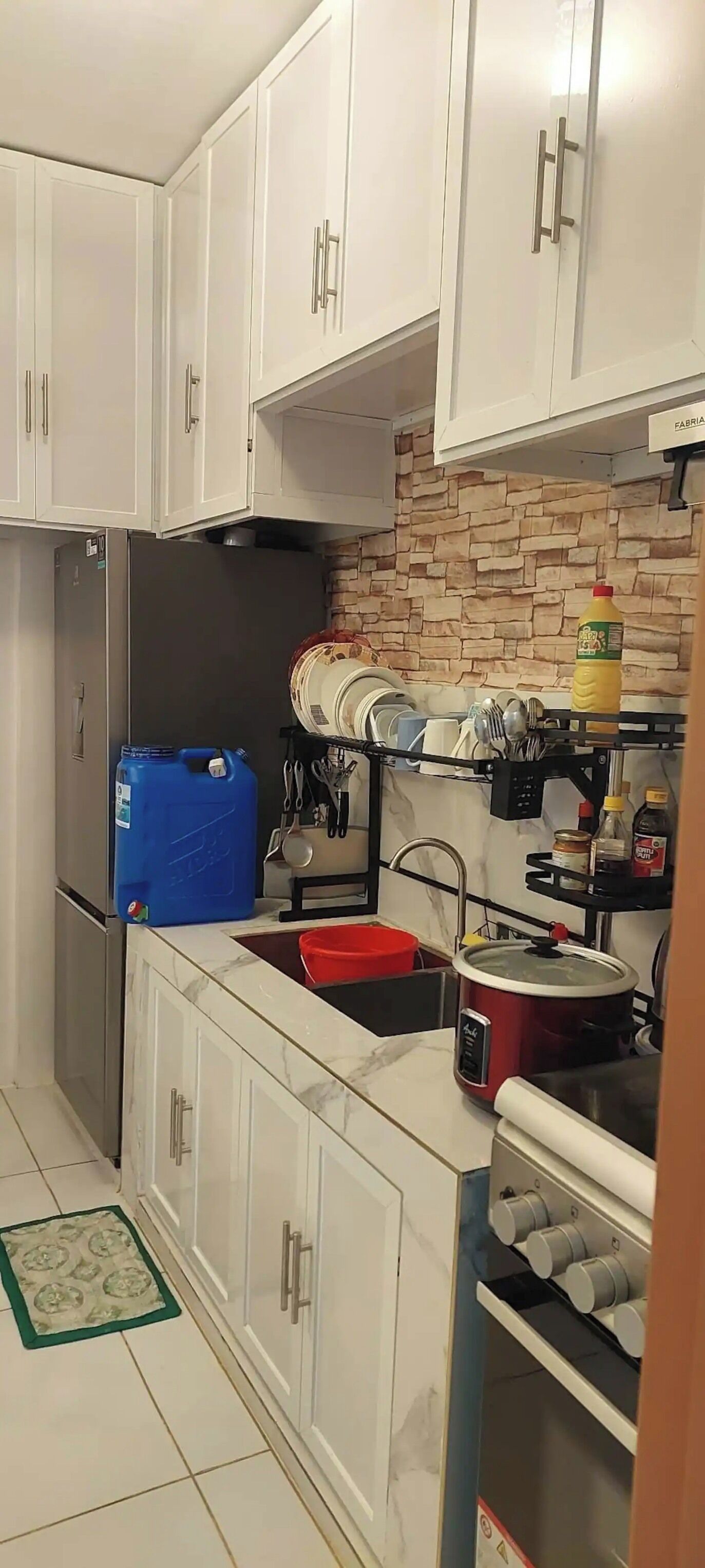 Una cocina con armarios blancos, un refrigerador de acero inoxidable, una olla roja y un recipiente azul.