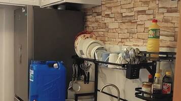Una cocina con armarios blancos, un refrigerador de acero inoxidable, una olla roja y un recipiente azul.