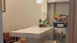 A compact kitchen with a white countertop, hanging pendant lights, a wooden chair, and a blue storage bin.