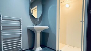 A bathroom with a pedestal sink, a white towel rack, a mirror, and a door leading to another room.