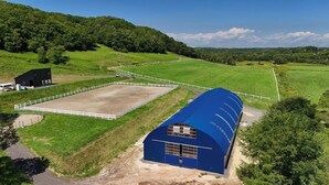 A large barn with a blue roof, surrounded by green fields and a white fence.