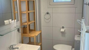 Ein Badezimmer mit einem weißen Waschbecken, einer Toilette, einem Holzregal und einem Fenster über der Toilette.