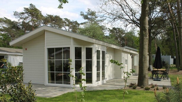 Ein modernes, eingeschossiges Haus mit großen Schiebeglastüren, einer überdachten Terrasse und einem gepflegten Rasen.