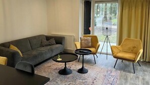 Ein modernes Wohnzimmer mit einer Couch, zwei Sesseln, einem Couchtisch und einem großen Fenster mit Vorhängen.