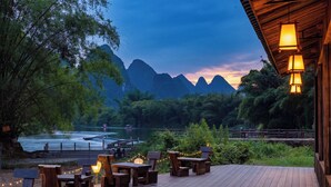 A wooden deck with outdoor seating, overlooking a river and mountains. - L'Eau Vive de Qixi Meidi Yangshuo- Riverfront Infinity Pool & Log Cabin Cafe (Guilin)