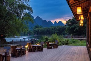 A wooden deck with outdoor seating, overlooking a river and mountains. - Qixi Meidi Yangshuo's Living Water (Guilin)