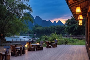 Una terraza de madera con mobiliario exterior, con vistas a un río y montañas.