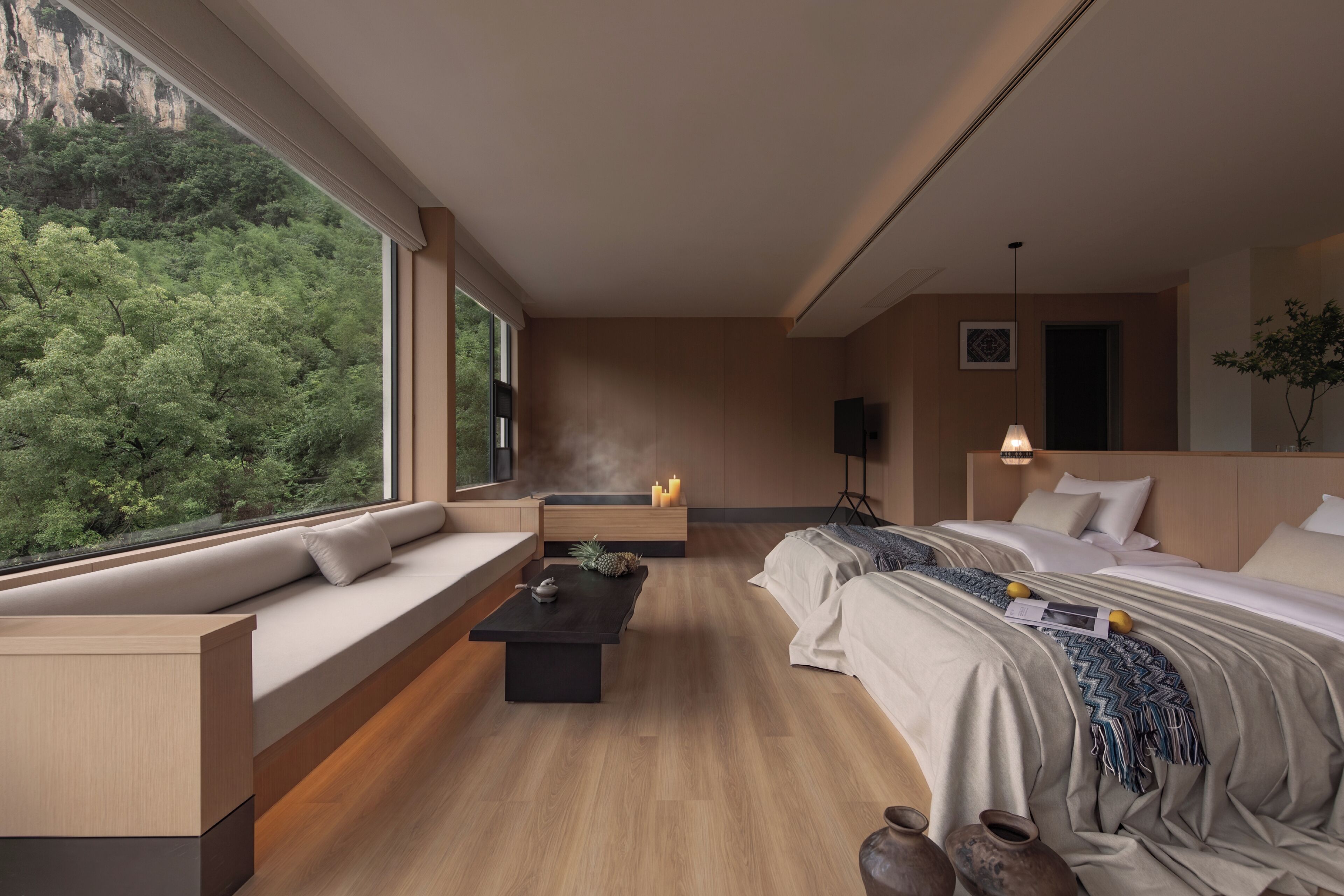 Una habitación de hotel moderna con un ventanal grande, un sofá, una cama, una mesita y una mesita de noche.