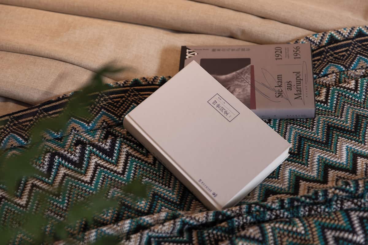 A book titled 'Sire Kam aus Mariupol 1920-1956' on a patterned fabric surface.