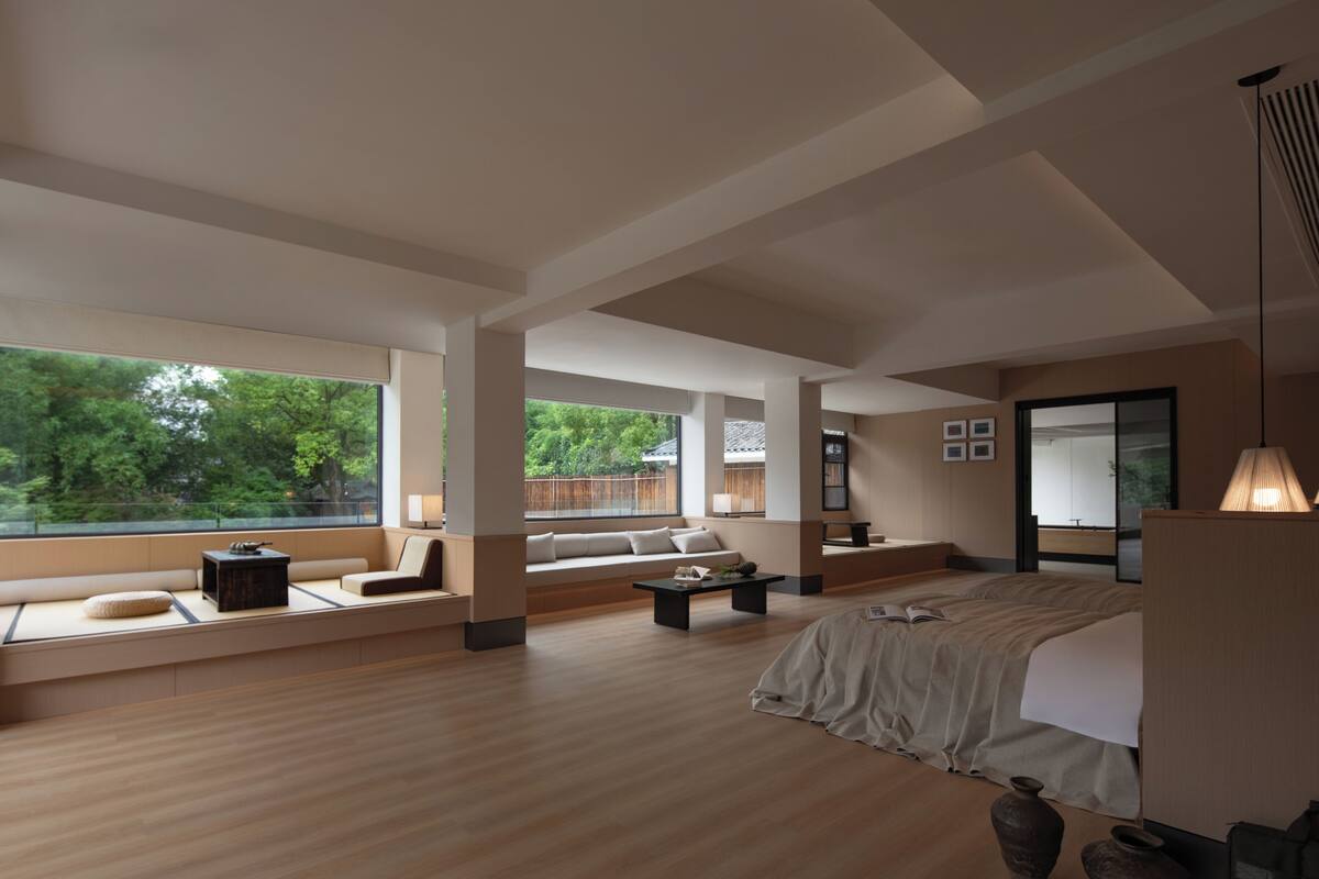 A modern hotel room with a large window, a bed, a sofa, and a small table.
