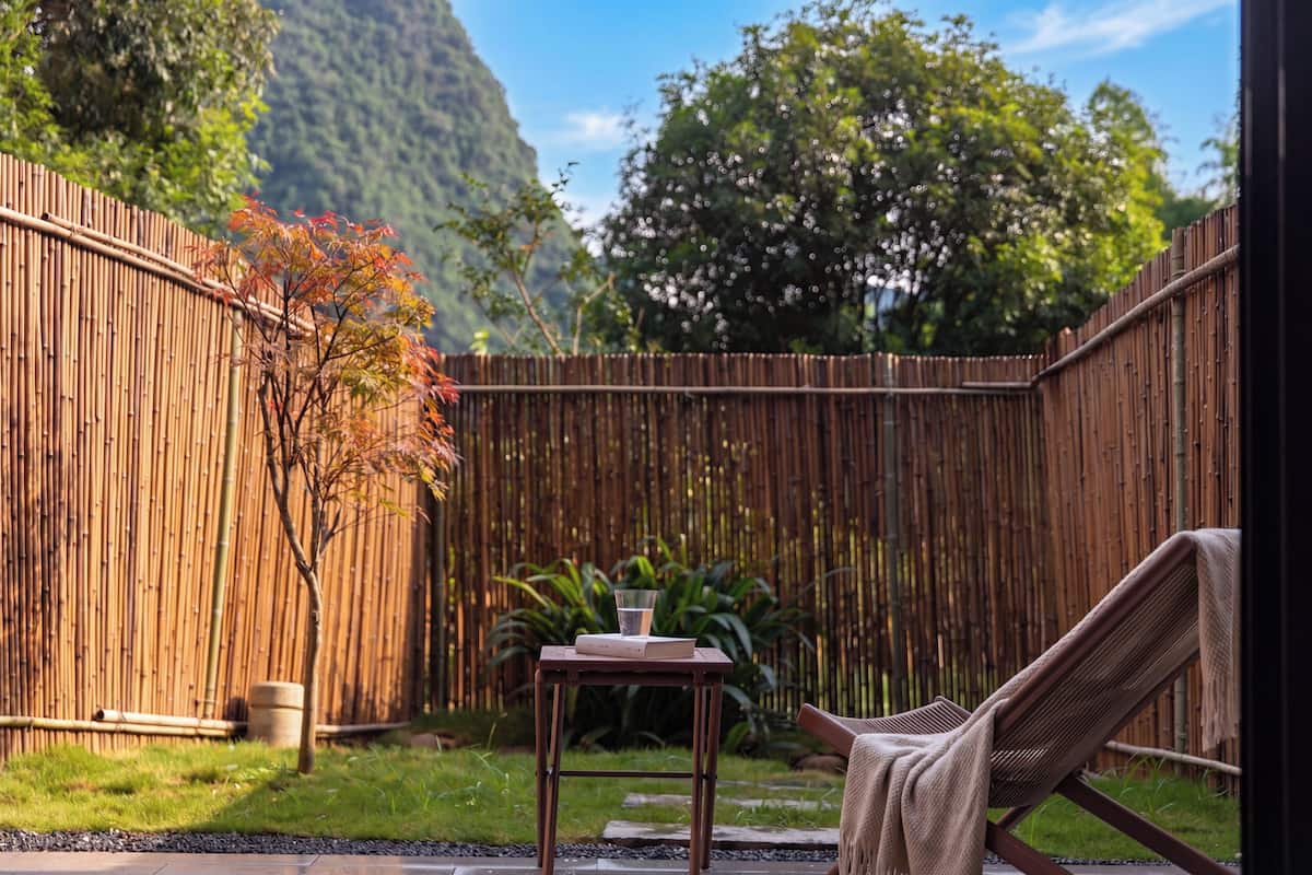 A bamboo fence, a small table with a glass, a chair, and a view of a mountain.