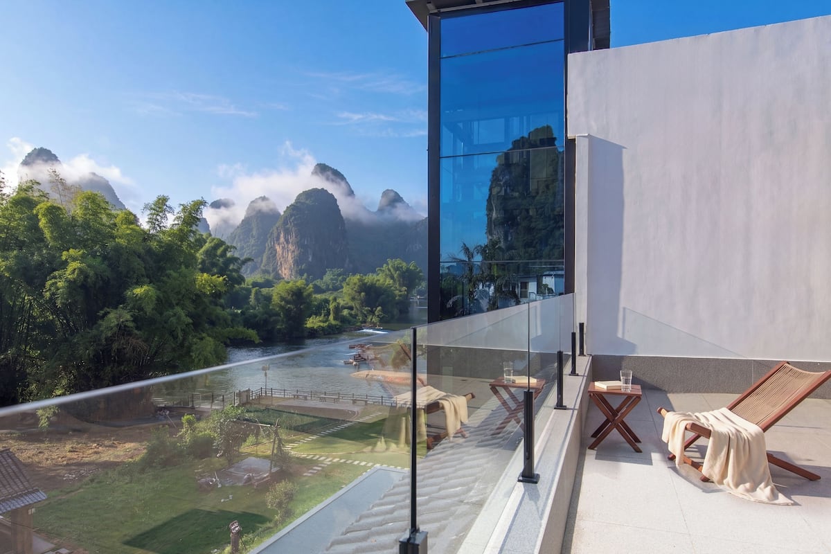 A balcony with a view of a river, lush greenery, and mountains.