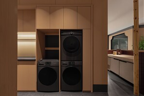 A modern laundry room with two front-loading washing machines, wooden cabinetry, and a countertop with a sink. - Qixi Meidi Yangshuo's Living Water (Guilin)