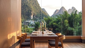 A dining area with a table set for four, large windows offering a view of mountains and greenery. - L'Eau Vive de Qixi Meidi Yangshuo- Riverfront Infinity Pool & Log Cabin Cafe (Guilin)