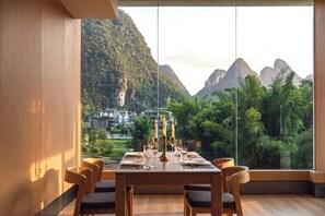 A dining area with a table set for four, large windows offering a view of mountains and greenery. - Qixi Meidi Yangshuo's Living Water (Guilin)