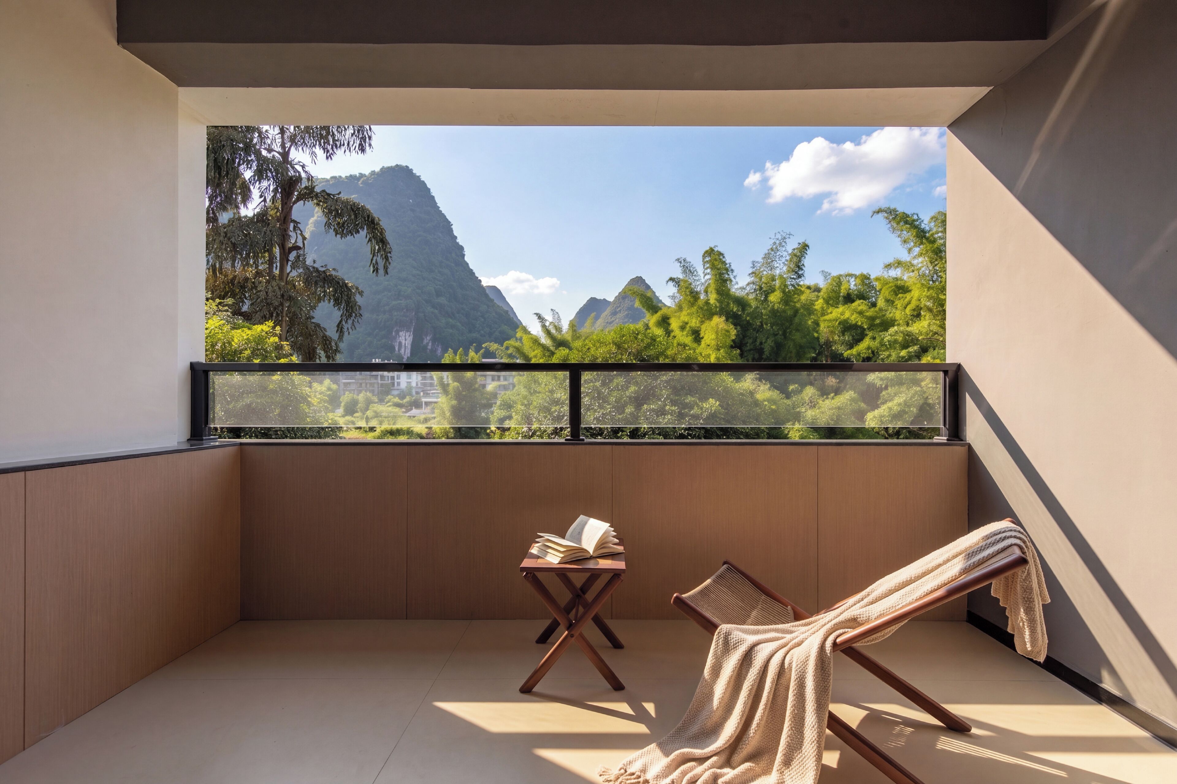 A balcony with a view of mountains, a wooden chair, a small table with a book, and a towel.