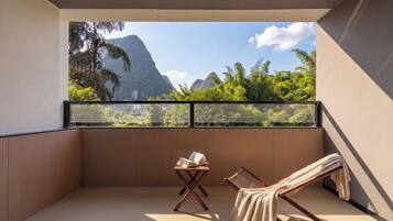 A balcony with a view of mountains, a wooden chair, a small table with a book, and a towel.