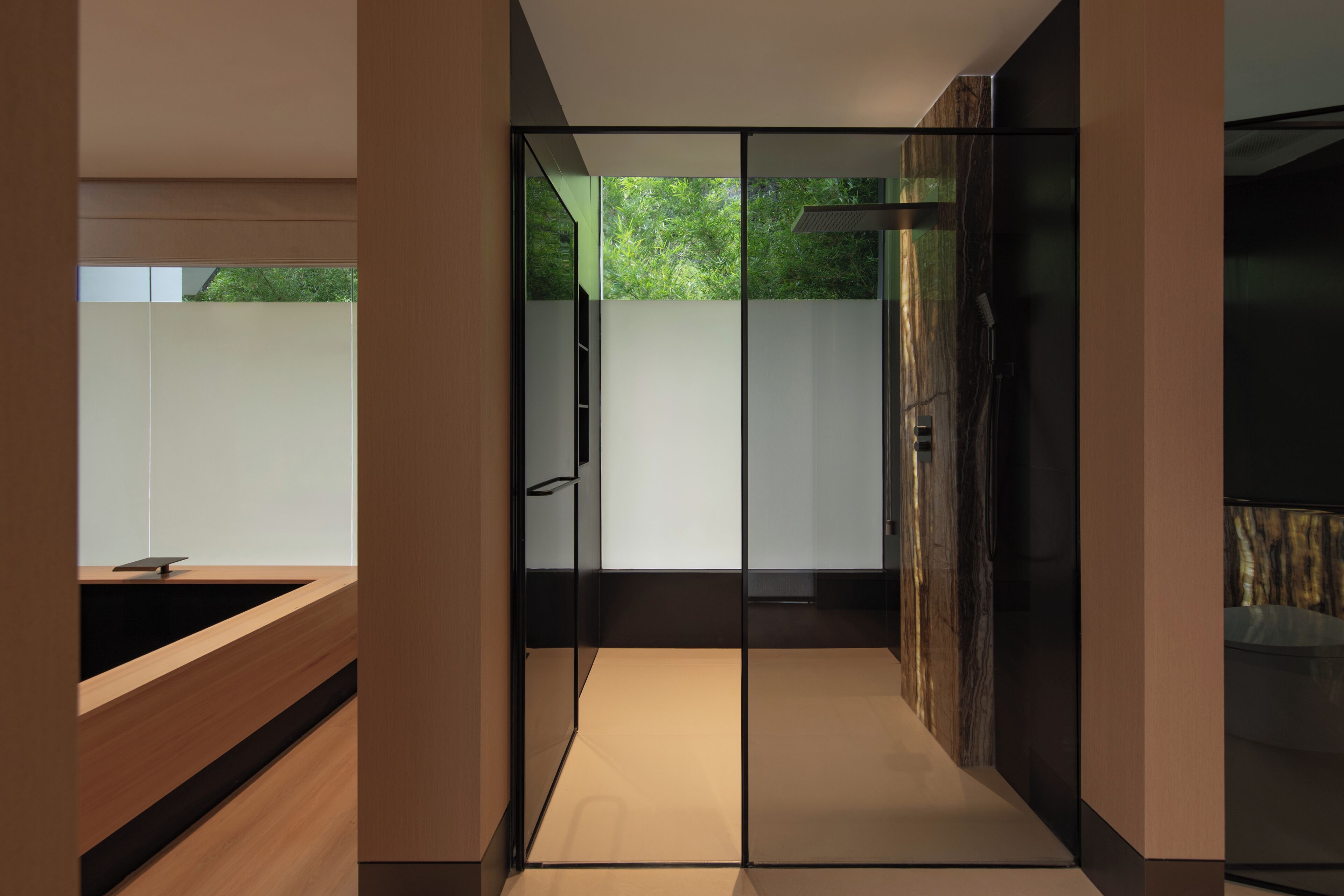 A modern interior with a glass partition, a wooden bench, and a view of greenery outside.