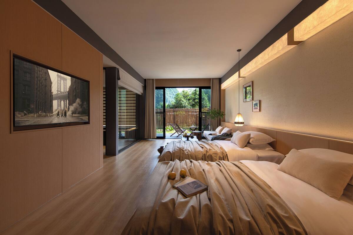 Moderni hotellihuone, jossa on suuri ikkuna, sänky, sohva ja ruokailutila, josta on näkymä vehreään maisemaan.
