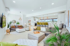 A modern living room with a sofa, ottoman, and a dining area with chairs.