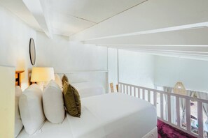 A hotel room with a bed, a nightstand with a lamp, a view of the balcony, and a window with curtains.
