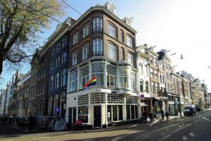 Een meerhoog gebouw met een opvallende hoekingang, een vlag en een tramlijn.