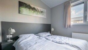 A hotel room with a bed, two bedside lamps, a painting on the wall, and a window with curtains. - Holiday Home in Arnhem With Terrace (Arnhem)