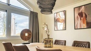 A dining area with a wooden table, leather chairs, a woven light fixture, and framed artwork on the walls. - Holiday Home in Arnhem With Terrace (Arnhem)