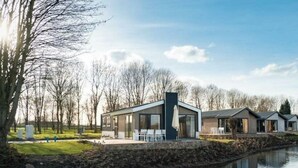 A modern building with a glass facade, a patio area with chairs, and a reflection in the water. - Holiday Home in Arnhem With Terrace (Arnhem)