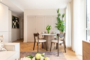 Ein modernes Wohnzimmer mit einem runden Esstisch, zwei Holzsesseln, einer Couch und einer großen Kühlpflanze.