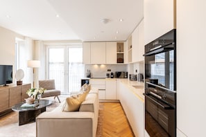 Eine moderne Küche mit eingebautem Ofen, ein Essbereich mit einer Couch und einem Couchtisch sowie ein Fernseher auf einem Holzschrank.
