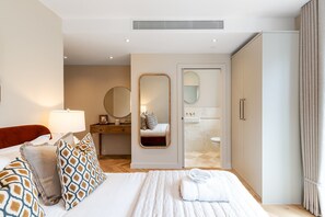 Ein Hotelzimmer mit Bett, Nachttisch, Lampe, Spiegel, Kleiderschrank und einem Badezimmer mit Waschbecken und Toilette.