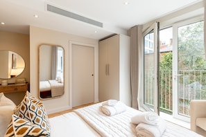 Ein modernes Schlafzimmer mit einem großen Bett, einem Schminktisch, einem Spiegel und einer Schiebetür zu einem Balkon.