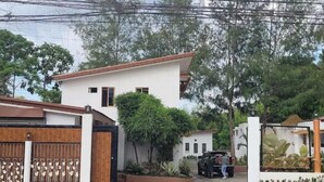 A modern two-story house with a gated entrance, a driveway, and a vehicle parked outside.