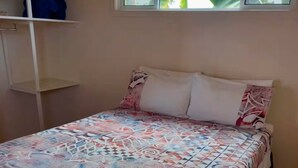 Una cama con colcha estampada, una ventana con vistas a zonas verdes y un estante blanco.