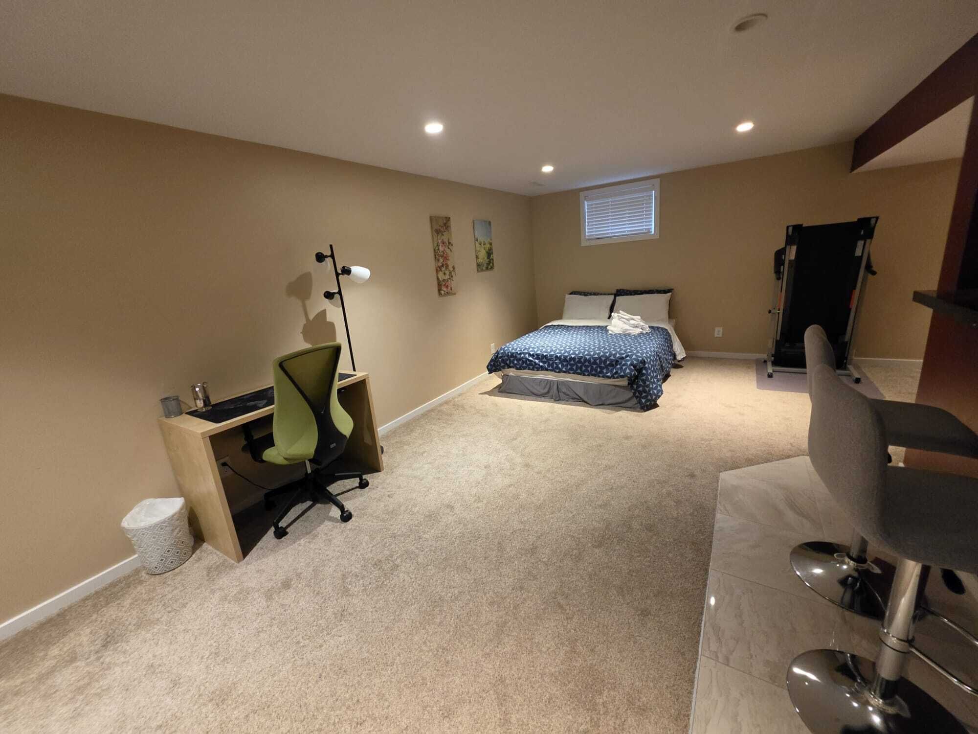 A bedroom with a bed, desk, chair, and exercise equipment.
