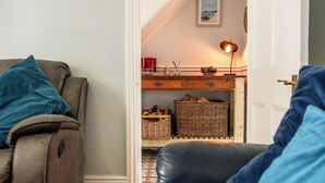 Ett vardagsrum med en soffa, en fåtölj, en lampa, korgar av rotting och en inramad tavla på väggen.