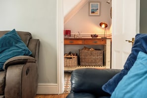 Ein Wohnzimmer mit einer Couch, einem Relaxsessel, einer Lampe, Weidenkörben und einem gerahmten Bild an der Wand.