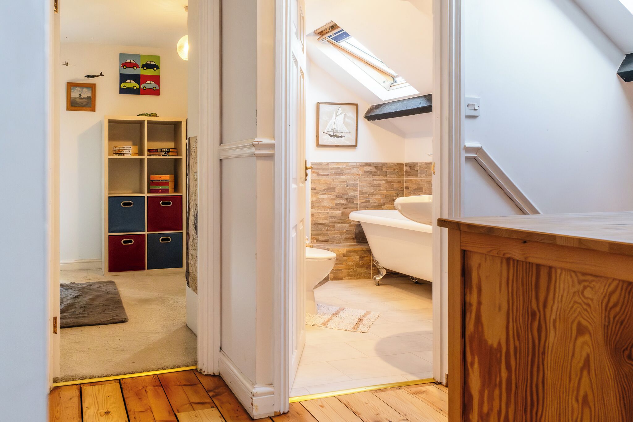 Un baño con bañera, suelo de madera, pared blanca y tragaluz.
