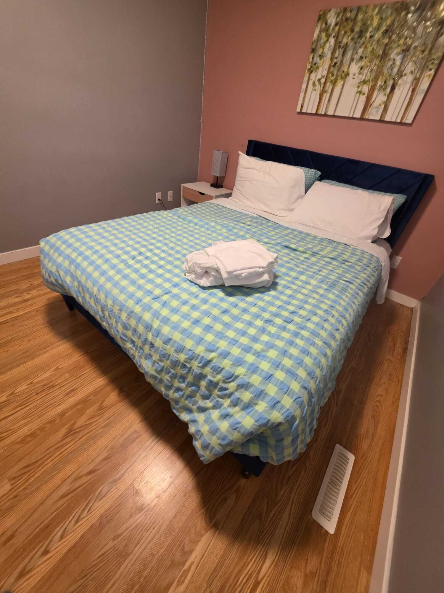 A neatly made bed with a checkered bedspread, a white pillow, and a folded white towel on the bed.