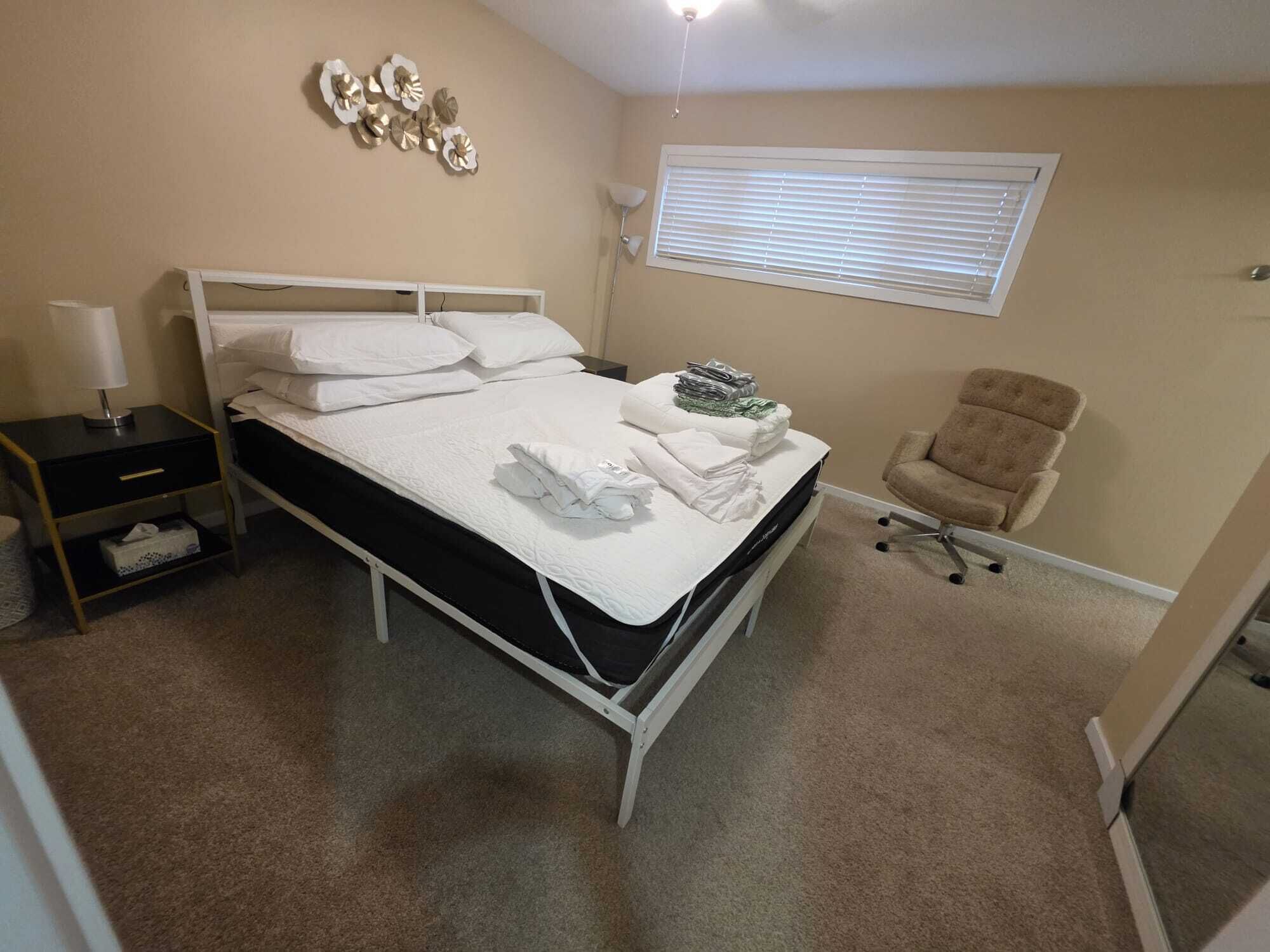 A bedroom with a bed, bedside table, lamp, chair, and window.