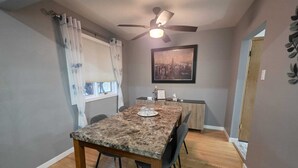 A dining area with a marble table, chairs, a ceiling fan, and a cityscape painting on the wall.
