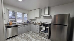 A modern kitchen with stainless steel appliances, a dishwasher, and a window with blinds.
