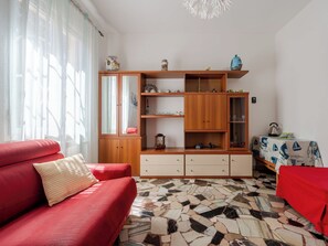 A living room with a red sofa, a wooden cabinet with glass doors, a tiled floor, and a table with a tablecloth. - A c à du Piero by Interhome (Albisola)