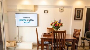 A dining area with a wooden table, chairs, a vase of flowers, and a screen displaying 'amazon prime video'. - Fully furnished apartment, beaches, between Monaco and Menton (Roquebrune-Cap-Martin)